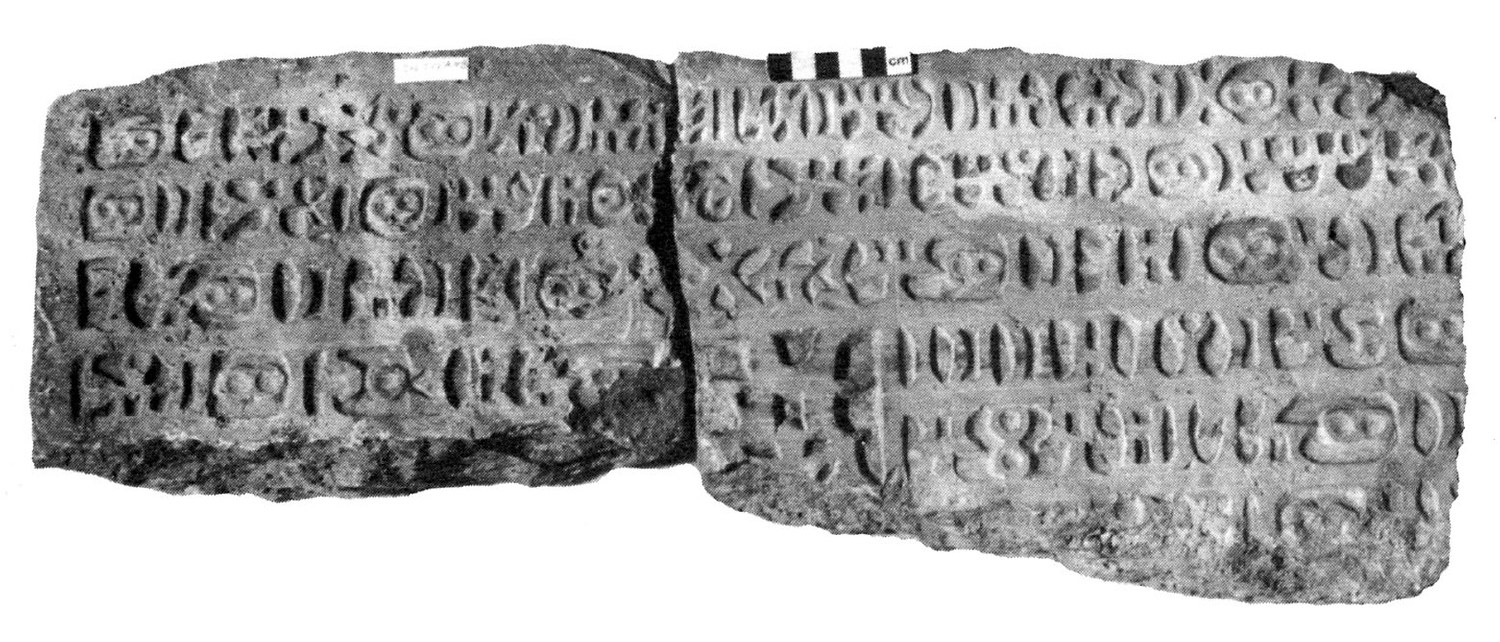 Black-and-white photograph of the CIH 543 stone in two joined pieces: four lines of raised South Arabian letters on the left piece and five on the right, with a centimetre scale bar along the top edge