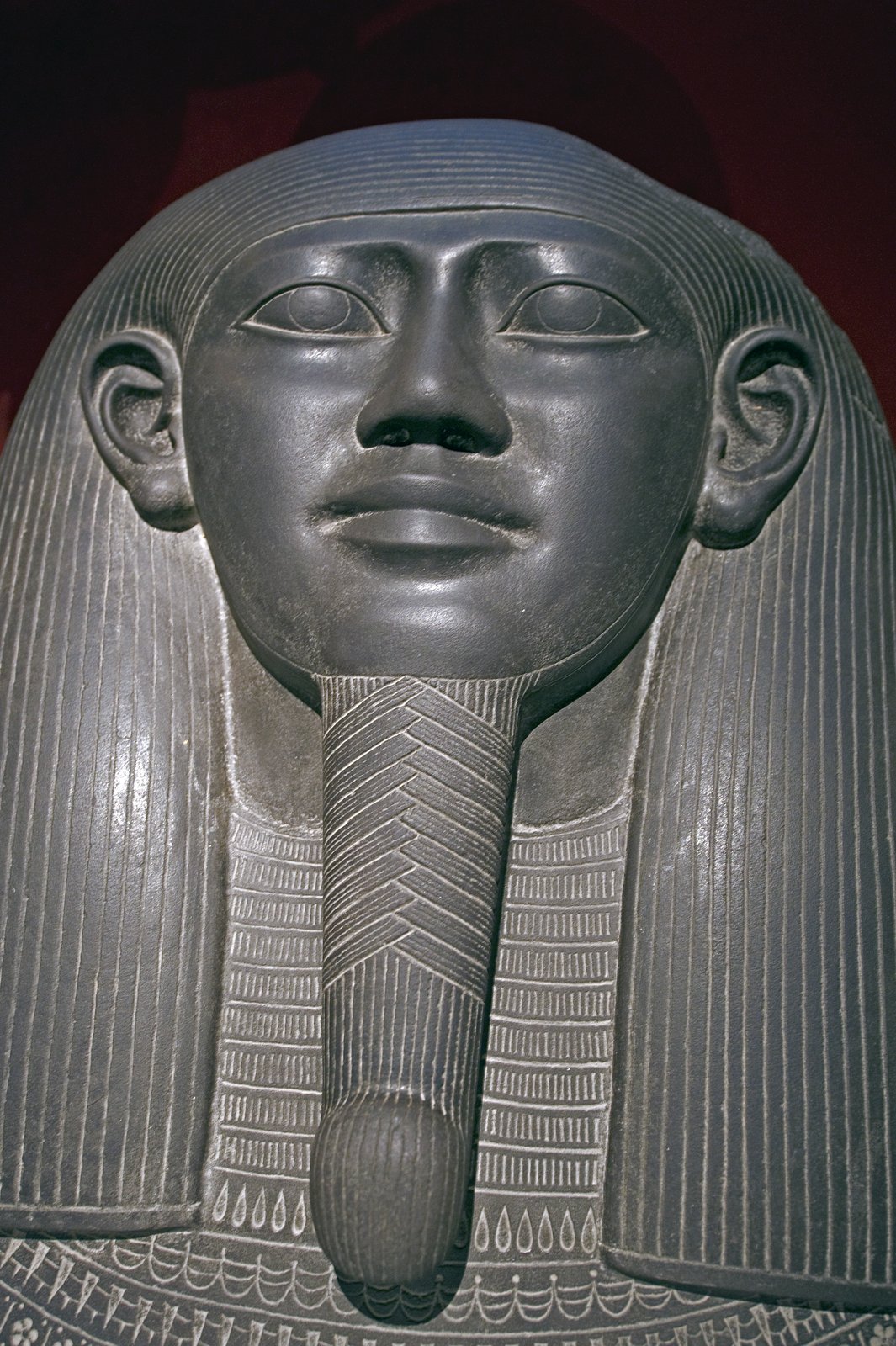 Close-up of the sarcophagus head: a carved Egyptian face with a long braided beard and a striated wig